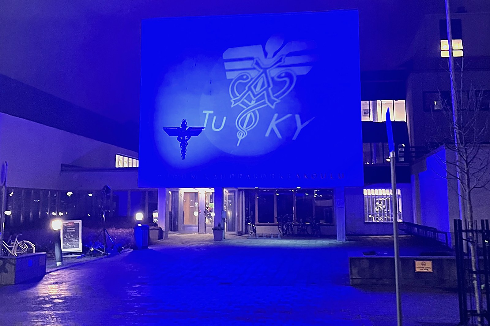 Kauppakorkeakoulun sisäänkäynti iltavalaistuksessa, julkisivulla TuKY:n tunnus.